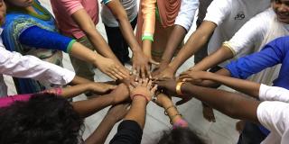A group of Bangladeshi young people stand in a circle and place their hands in the centre