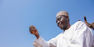 A male farmer runs grain through his hands against a bright blue sky