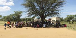 A large group of parents gather under a tree as children begin a dance performance at Archerer primary school