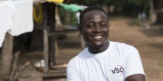 Community volunteer James smiles as he stands outside, behind one of the bamboo drying racks he's making