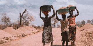 Women carry basins down a track in Rhino Camp, Uganda.