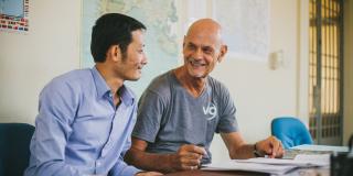 Volunteer Wim Lancsweert and local colleague Heng Eak sit at a desk together, discussing plans for improving education system administration