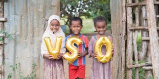 Children hold balloons in front of a wooden gate in Ethiopia.