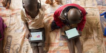 Two young schoolchildren sit on the floor at Mdzobwe Primary School and use their tablets to learn