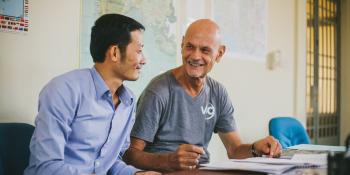 Volunteer Wim Lancsweert and local colleague Heng Eak sit at a desk together, discussing plans for improving education system administration