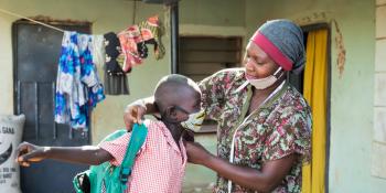 Seamstress helps a schoolchild put on a mask she made