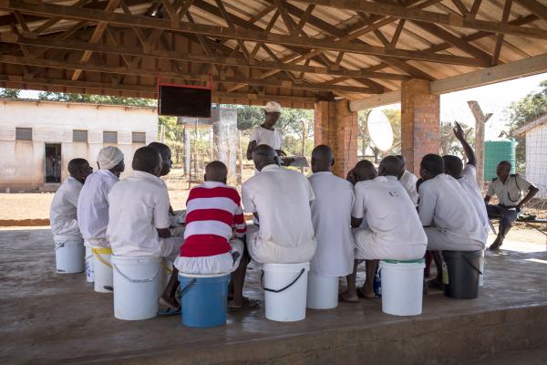A group of male prisoners sit in a circle listening to a peer educator speak about health issues