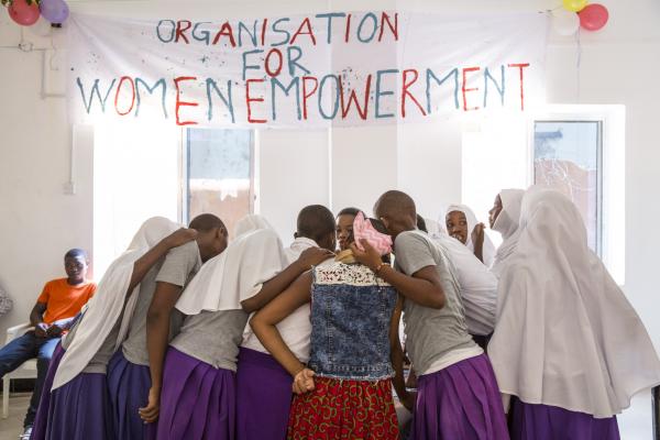 A group of girls huddle together under a sign reading 'Organisation for women empowerment'