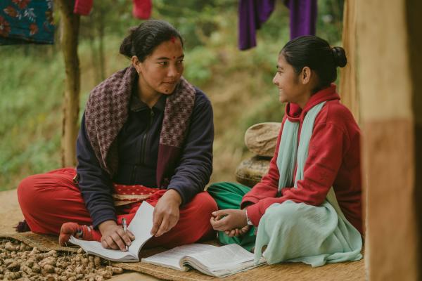 Big Sister Rama and Little Sister Pramila sit on a mat outside to study