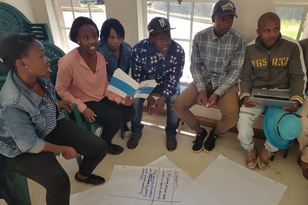 A group of young people sit in a circle on chairs, discussing the scores they are assigning to health services provided for them