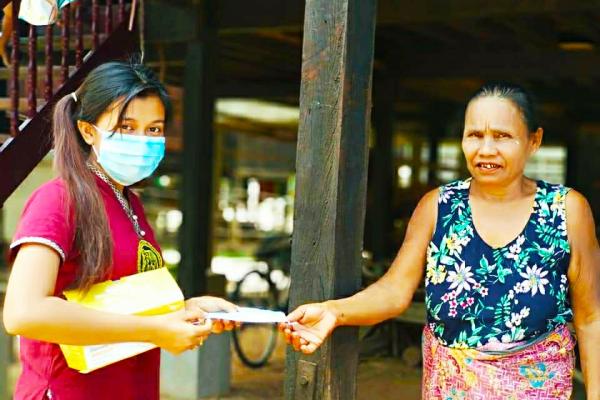 a young woman handing a mask over to an elderly woman 