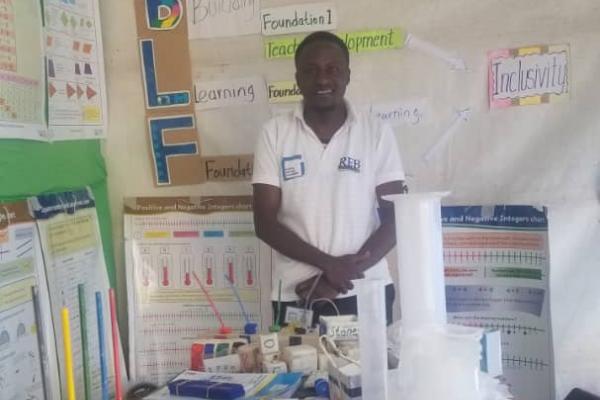 VSO volunteer Dennis Bwire standing by a desk with learning materials.