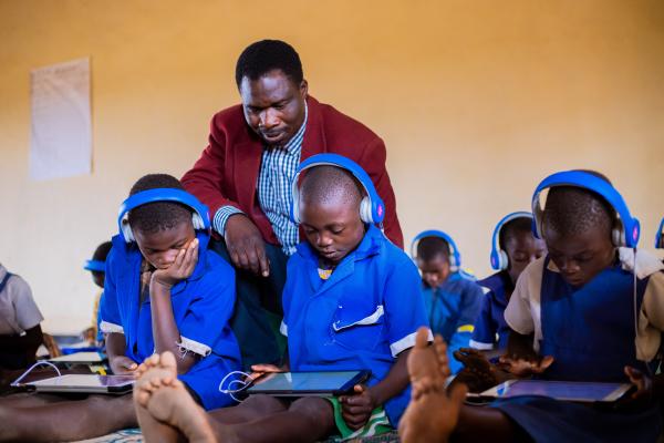 Theonas sits in the learning centre helping students on their tablets