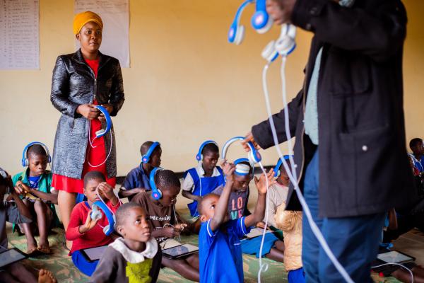 VSO volunteer Prisca and VSO volunteer Theo handing out tablets and headsets to students.