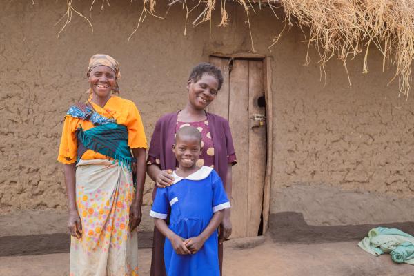 Alinafe standing with her two grandmothers outside their home.